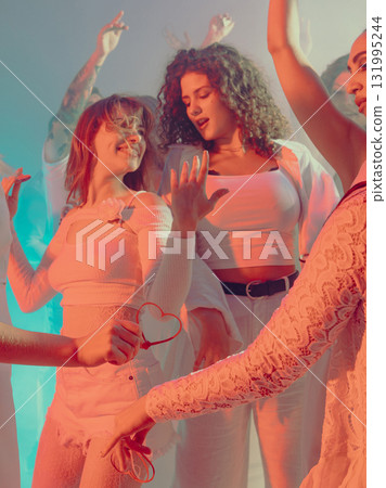 Women dancing joyfully at white party in warm romantic light. 131995244