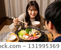 A woman and her husband sit around a kotatsu and pick ingredients for a hot pot dish 131995369