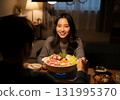 A woman and her husband smile around a warm earthenware pot in a dark room 131995370