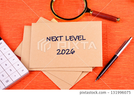 On a wooden orange background, several beige envelopes sit with NEXT LEVEL and 2026 written. Beside it, there is a calculator, pen, and magnifying glass 131996075