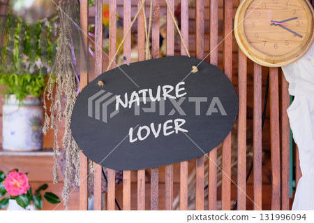 A black oval sign hangs, proclaiming Nature Lover. The setting is a rustic indoor space. Dried florals and plants adorn shelves, adding to the charming decor. A clock hangs nearby A black oval sign hangs, proclaiming Nature Lover. The setting is a rustic indoor space. Dried florals and plants adorn shelves, adding to the charming decor. A clock hangs nearby 131996094
