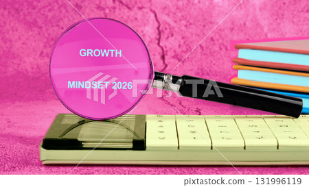A magnifier is placed over an old calculator, revealing the phrase growth mindset 2026. Stacks of colorful books are nearby, all on a textured pink surface 131996119