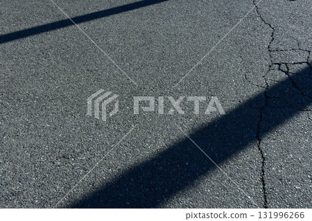 Cracked asphalt and two diagonal black shadows. Urban background material Cracked asphalt and two diagonal black shadows. Urban background material 131996266
