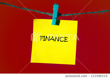 A bright yellow note with the word Finance is clipped to a string against a stark red backdrop. It suggests reminders or importance of money management A bright yellow note with the word Finance is clipped to a string against a stark red backdrop. It suggests reminders or importance of money management 131996319
