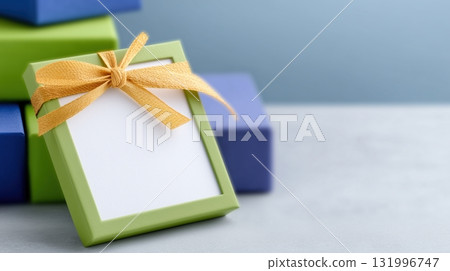 Green Gift Box with Golden Ribbon and Blank Label on Grey Background 131996747