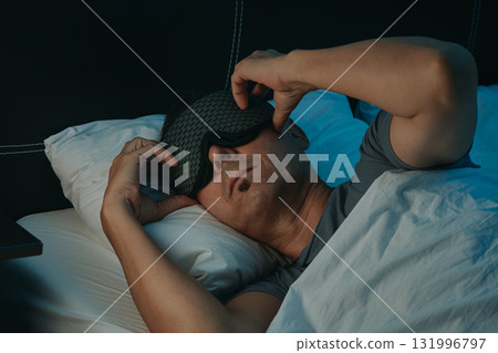 closeup of a man in bed adjusting his sleep mask closeup of a man in bed adjusting his sleep mask 131996797