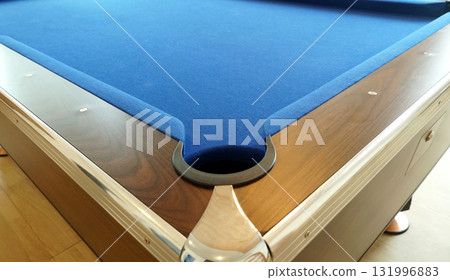 A hole in the corner of a pool table with a wooden border. and covered with a blue flannel cloth. A hole in the corner of a pool table with a wooden border. and covered with a blue flannel cloth. 131996883