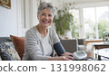 smiling woman measuring blood pressure with modern digital device in living room 131998062