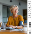 middle aged woman using blood pressure monitor on desk with soft daylight 131998067