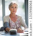 middle aged woman using blood pressure monitor on desk with soft daylight 131998068