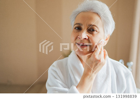 Mature adult old woman doing daily beauty routine removing makeup with cotton pad. Senior woman with lotion sponge washing face gets facial treatment. Skin care aging beauty skincare cleansing 131998839