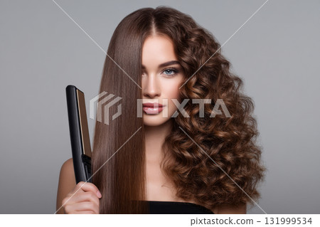 Woman styling her hair with a flat iron, showing half straight and half curly 131999534