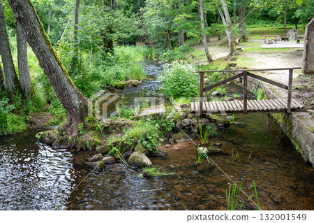 A tranquil and peaceful stream gently flows through vibrant greenery, featuring a charming wooden bridge for crossing 132001549