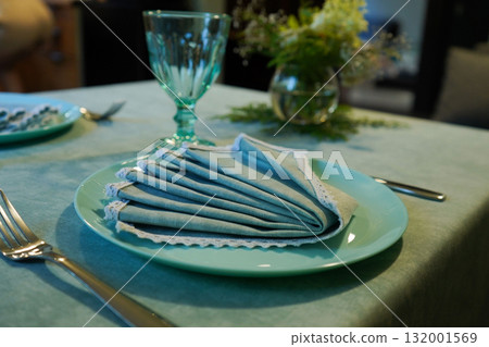 The table features a charming arrangement, with a crisp napkin carefully placed on the plate, ready for guests to enjoy their meal. The table features a charming arrangement, with a crisp napkin carefully placed on the plate, ready for guests to enjoy their meal. 132001569
