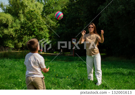 Playing ball game with family. Serene moment of connection as mother and son. Warm sunlight and grassy field highlight quality family time. Playing ball game with family. Serene moment of connection as mother and son. Warm sunlight and grassy field highlight quality family time. 132001613