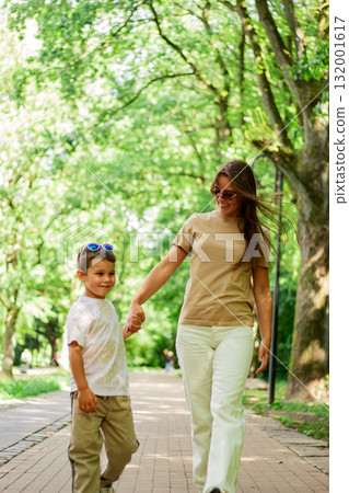 Caucasian mother and son enjoy leisure time in park walking and talking, smiling laughing. Serene family connection. 132001617
