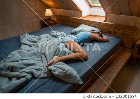 In a serene attic bedroom, a person is peacefully resting among soft and cozy bedding, surrounded by tranquility 132001654
