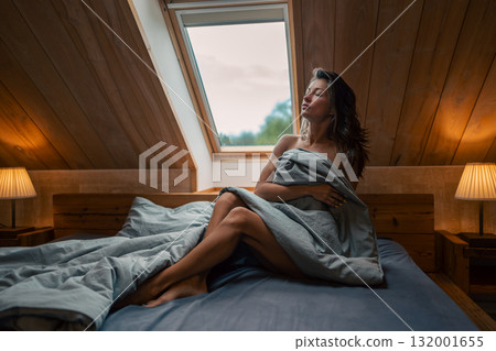 A serene morning shows a woman cozy in a warm blanket by the window, enjoying the tranquility of the moment A serene morning shows a woman cozy in a warm blanket by the window, enjoying the tranquility of the moment 132001655
