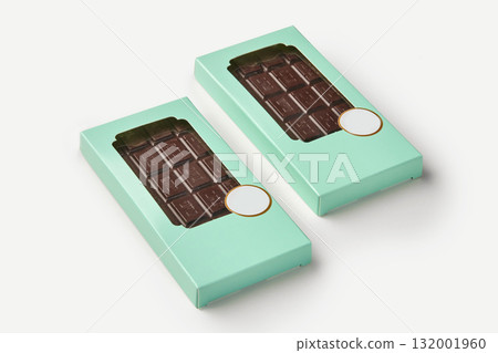 Two dark chocolate bars resting in light green boxes on white background 132001960