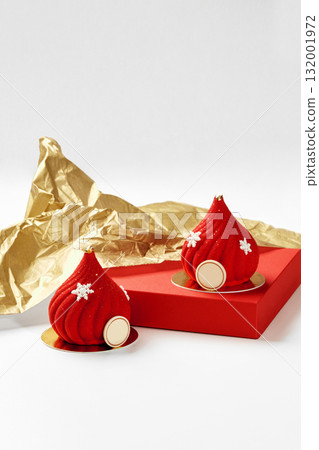 Two red christmas mousse cakes decorated with snowflakes and gold details resting on red surface with gold wrapping paper Two red christmas mousse cakes decorated with snowflakes and gold details resting on red surface with gold wrapping paper 132001972