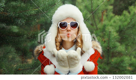 Happy young woman in winter park against Christmas tree, girl in white hat, glasses in snowy forest Happy young woman in winter park against Christmas tree, girl in white hat, glasses in snowy forest 132002081