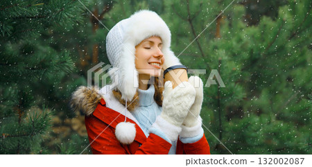 Winter day, happy smiling woman holding cup of coffee drink enjoys snow, against Christmas tree Winter day, happy smiling woman holding cup of coffee drink enjoys snow, against Christmas tree 132002087