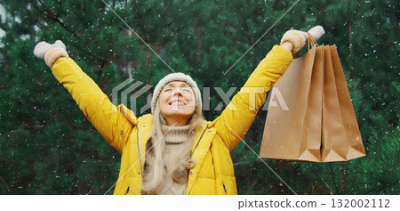 Happy smiling young woman with shopping bag in winter against Christmas tree, holiday shopping Happy smiling young woman with shopping bag in winter against Christmas tree, holiday shopping 132002112