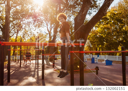 Fit mid adult ginger headed woman push-ups from sports horizontal bar. Concept of sports and outdoor training Fit mid adult ginger headed woman push-ups from sports horizontal bar. Concept of sports and outdoor training 132002151