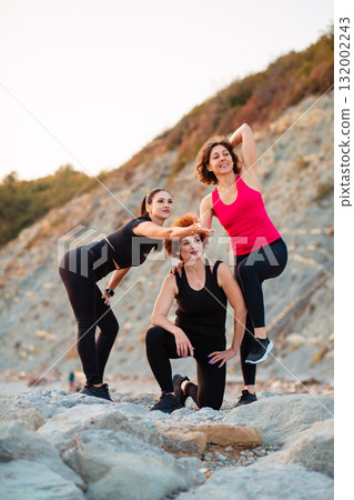 Three adult athletic Caucasian happy women in sportswear posing standing on rock. Vertical. Wellness and sport lifestyle Three adult athletic Caucasian happy women in sportswear posing standing on rock. Vertical. Wellness and sport lifestyle 132002243