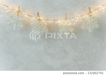 White Snowflake Ornaments Hanging on String Lights Against Textured Wall 132002742