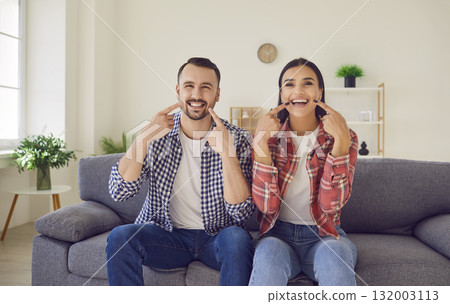 Young happy married couple sitting on the sofa in the living room at home and smiling. Young happy married couple sitting on the sofa in the living room at home and smiling. 132003113