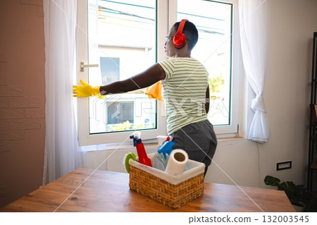 Woman cleaning windows while listening to music with headphones at home 132003545