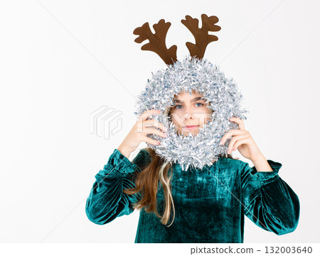 Cheerful teen girl in velvet dress brown reindeer antlers festive ornaments, celebrating holiday season on white background. 132003640