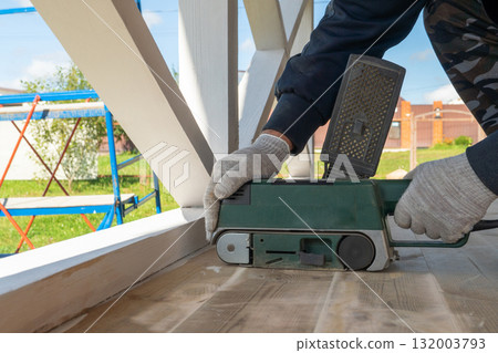 Carpenter smoothing wooden surface with belt sander outdoors 132003793