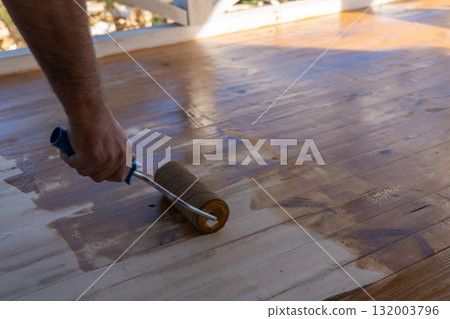 Close-up of male hand applying varnish with roller on wooden decking 132003796