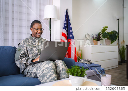 American female soldier working on laptop at home with United States flag in background American female soldier working on laptop at home with United States flag in background 132003865