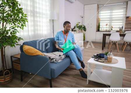 Nurse preparing for home visit, reviewing medical records on sofa 132003976