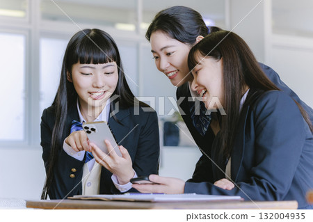 A high school girl talking to her classmate while looking at her smartphone in the classroom 132004935