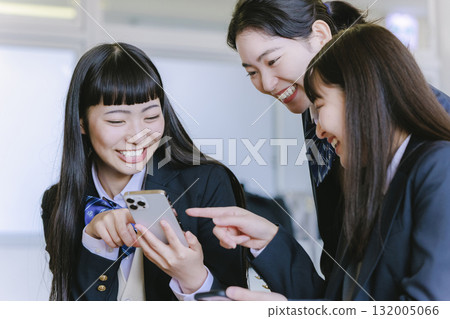 一個高中女生在教室裡一邊看著她的智能手機一邊和她的同學聊天 132005066