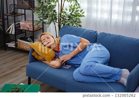 Exhausted nurse sleeping on sofa after long shift at hospital Exhausted nurse sleeping on sofa after long shift at hospital 132005262