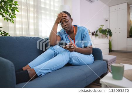 Tired nurse checking her phone sitting on the sofa at home after work Tired nurse checking her phone sitting on the sofa at home after work 132005270