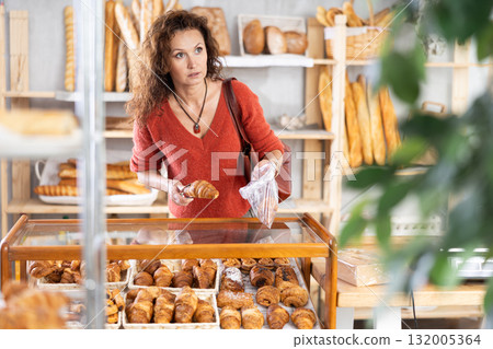 Woman putting croissants into plastic bag in bakery 132005364