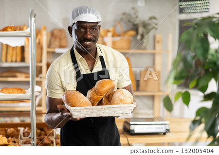 Male baker holding a tray of freshly baked bread in a bakery 132005404