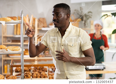 African man near window of bakery food court store examines assortment African man near window of bakery food court store examines assortment 132005437