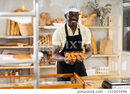 African male baker worker sells cookie, shows many products African male baker worker sells cookie, shows many products 132005496