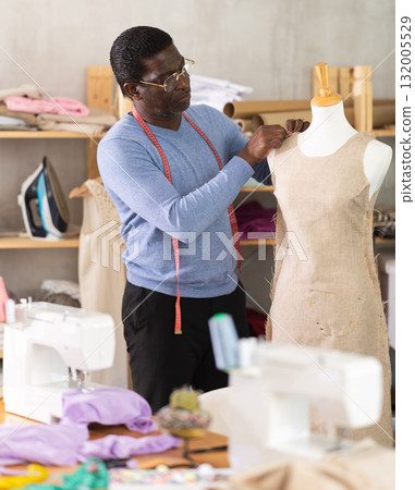 African American man tailor connects parts of dress on mannequin. African American man tailor connects parts of dress on mannequin. 132005529