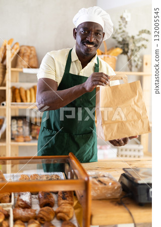 Smiling male baker presenting a takeaway paper bag 132005545