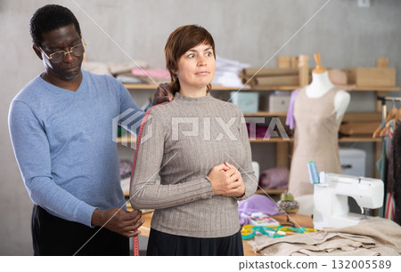 African American man tailor takes measurements from female client 132005589