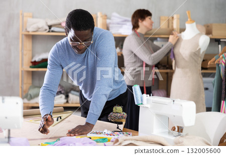 Male fashion designer drafting clothing pattern in studio with female colleague Male fashion designer drafting clothing pattern in studio with female colleague 132005600
