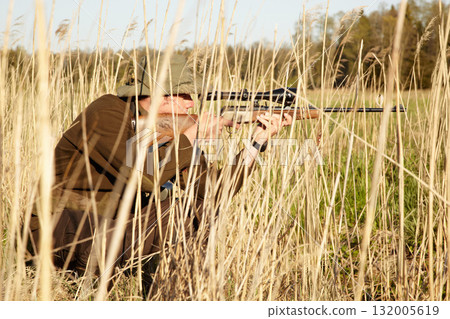 Nature, hunter and man with a rifle while in camouflage shooting in outdoor field. Grass, wildlife and male sniper hunting animals with shotgun weapon hiding in plants to shoot target in countryside. 132005619